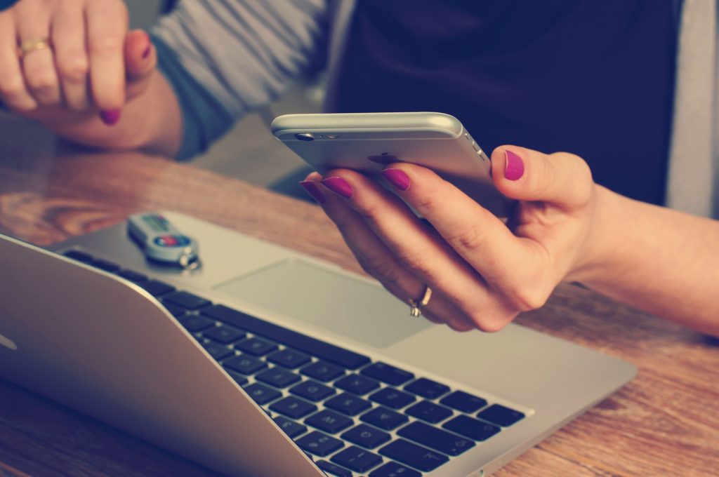 femme tenant un téléphone avec un pc devant